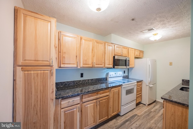 kitchen featuring a textured ceiling, white appliances, light hardwood / wood-style floors, and dark stone counters