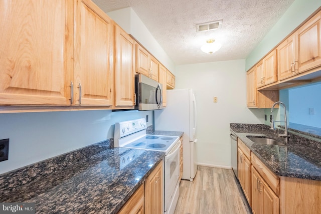 kitchen with dark stone counters, sink, light wood-type flooring, a textured ceiling, and appliances with stainless steel finishes