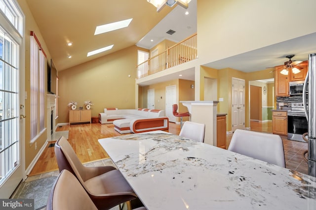 dining space featuring ceiling fan, a healthy amount of sunlight, a fireplace, and high vaulted ceiling