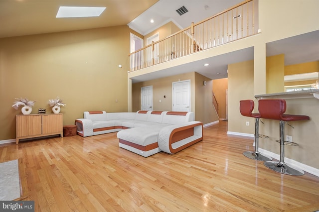 living room with a skylight, high vaulted ceiling, and light hardwood / wood-style floors