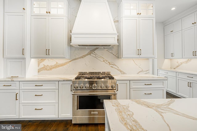 kitchen featuring high end range, decorative backsplash, custom range hood, light stone counters, and white cabinetry