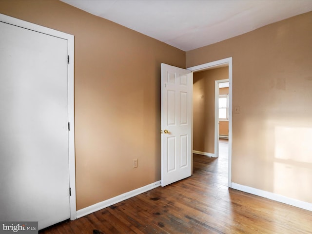 unfurnished bedroom with a baseboard radiator and dark wood-type flooring