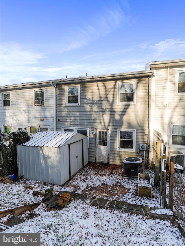 snow covered house featuring a shed and central AC unit