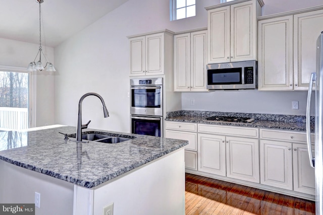 kitchen with stainless steel appliances, a kitchen island with sink, dark stone counters, and sink