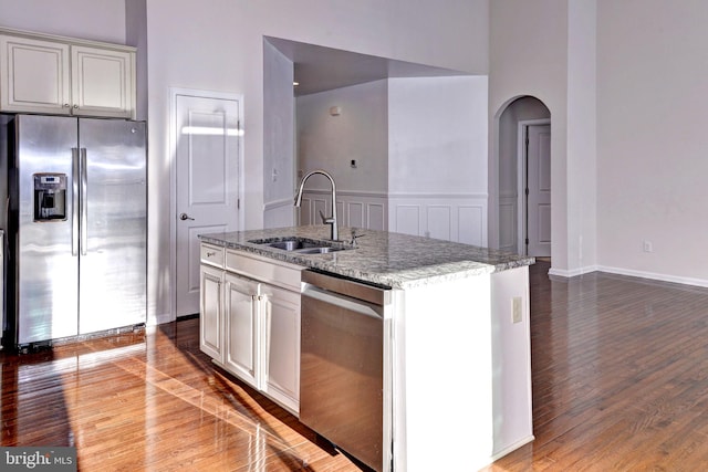 kitchen with a center island with sink, sink, light stone countertops, appliances with stainless steel finishes, and wood-type flooring