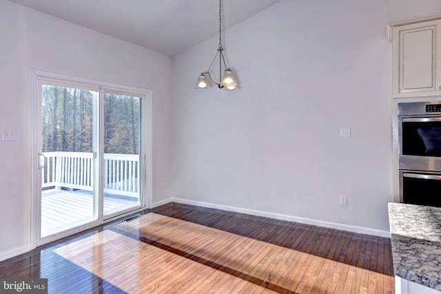 unfurnished dining area featuring lofted ceiling, dark hardwood / wood-style floors, and an inviting chandelier