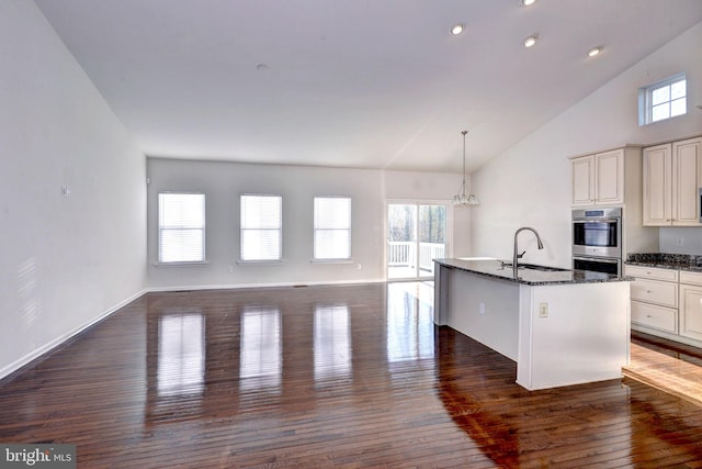 kitchen featuring stainless steel double oven, sink, dark stone countertops, dark hardwood / wood-style floors, and an island with sink