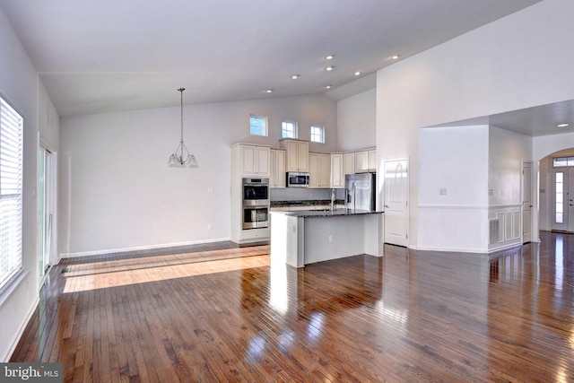 kitchen with a center island with sink, a towering ceiling, appliances with stainless steel finishes, decorative light fixtures, and wood-type flooring