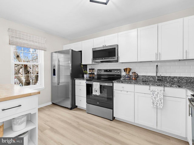 kitchen with light wood-style flooring, a sink, backsplash, stainless steel appliances, and white cabinets