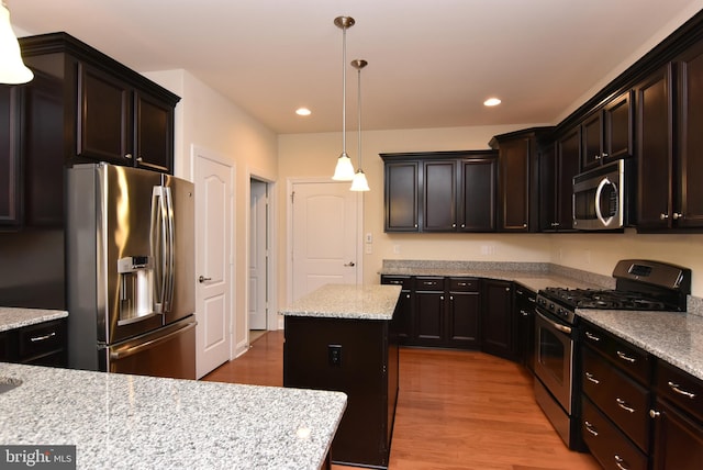 kitchen with appliances with stainless steel finishes, light stone counters, decorative light fixtures, a center island, and light hardwood / wood-style floors