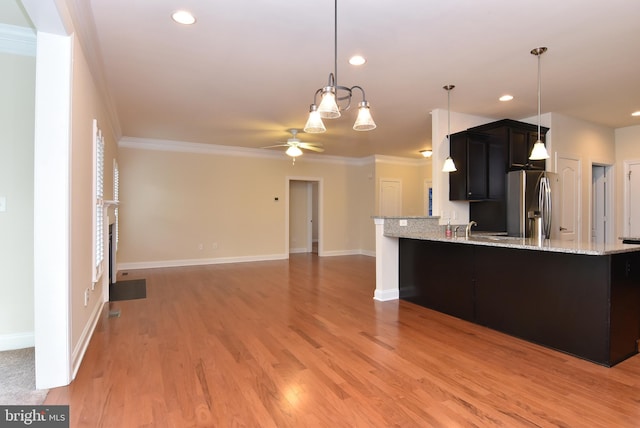 kitchen with kitchen peninsula, stainless steel refrigerator with ice dispenser, light stone counters, ornamental molding, and ceiling fan