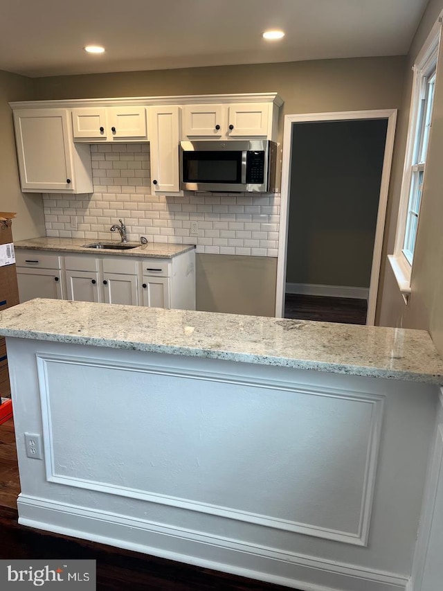 kitchen with backsplash, white cabinetry, sink, and light stone counters