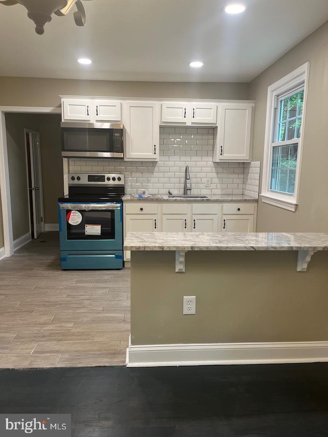 kitchen featuring light stone countertops, stainless steel appliances, sink, white cabinetry, and a breakfast bar area