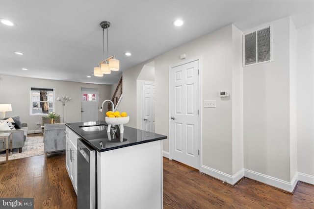 kitchen with white cabinets, decorative light fixtures, dark hardwood / wood-style flooring, sink, and a center island with sink