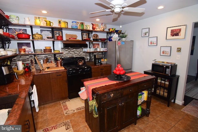 kitchen featuring stainless steel refrigerator, ceiling fan, black range with gas cooktop, decorative backsplash, and dark brown cabinets