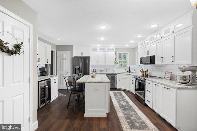 kitchen with white cabinets, a kitchen island, beverage cooler, and appliances with stainless steel finishes