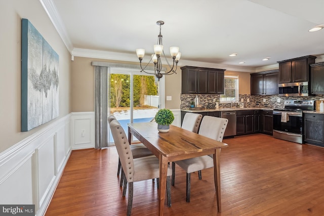 dining area with sink, a chandelier, dark hardwood / wood-style floors, and ornamental molding