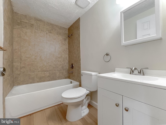 full bathroom featuring toilet, hardwood / wood-style flooring, a textured ceiling, tiled shower / bath combo, and vanity