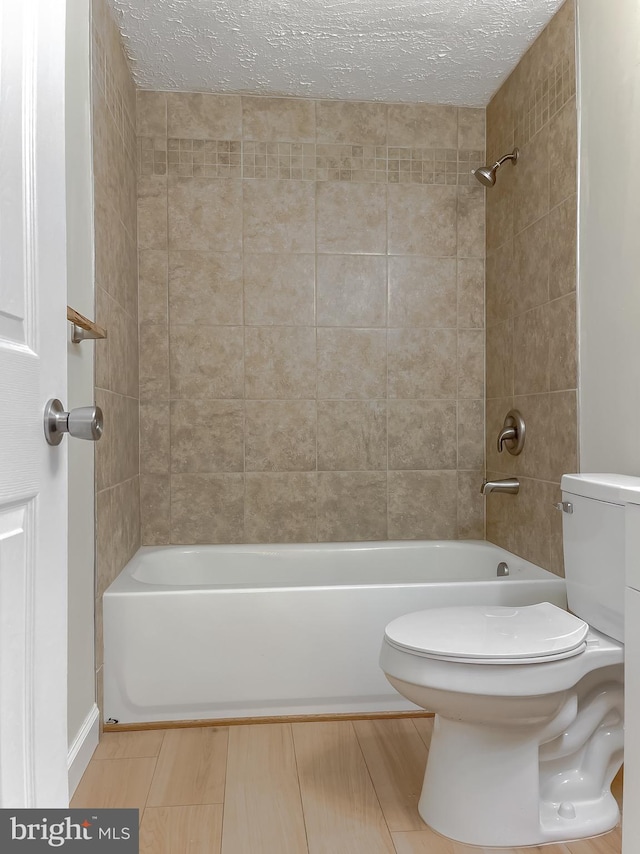 bathroom with toilet, a textured ceiling, and tiled shower / bath