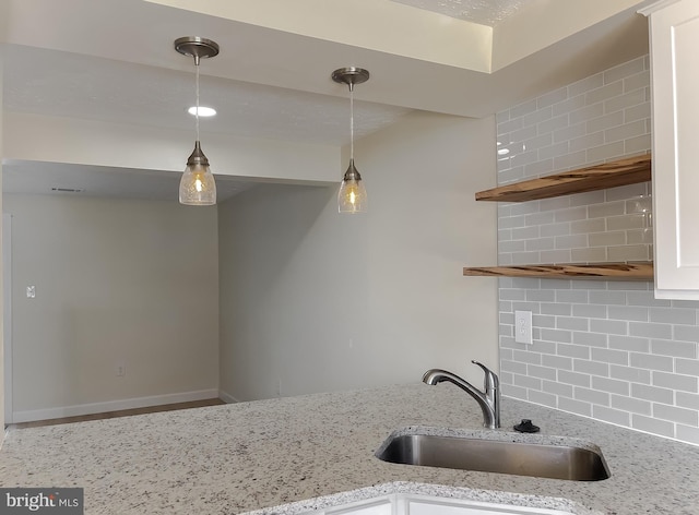 kitchen with sink, decorative light fixtures, light stone counters, and decorative backsplash