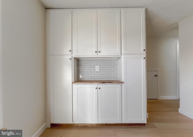 interior space featuring decorative backsplash, white cabinetry, light wood-type flooring, and a textured ceiling