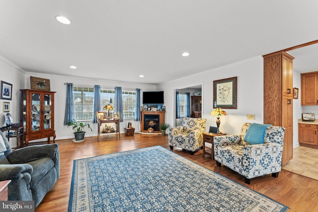 living area with a lit fireplace, recessed lighting, light wood-style flooring, and crown molding