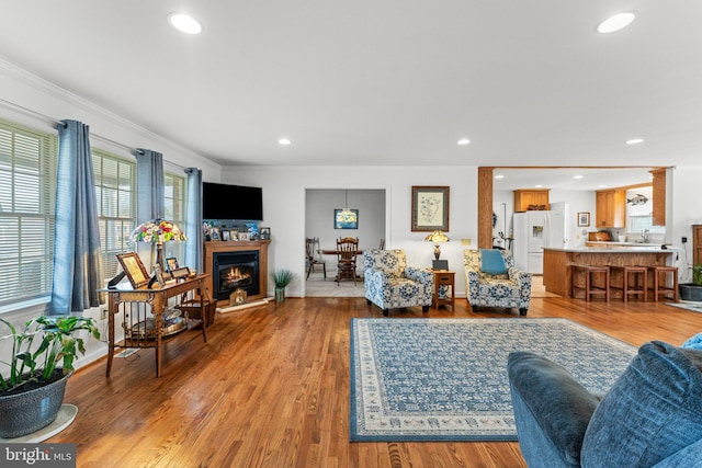 living room featuring recessed lighting, crown molding, a lit fireplace, and wood finished floors