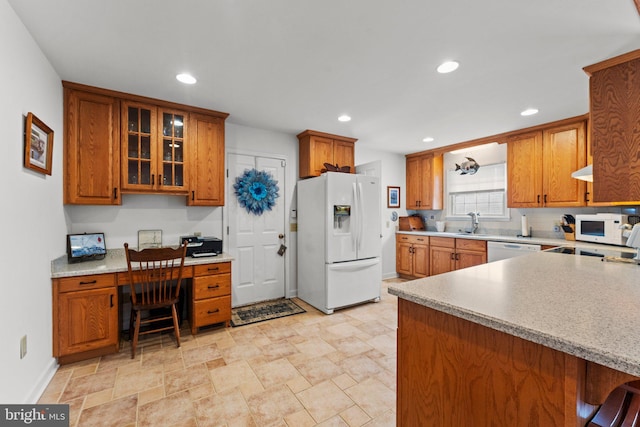 kitchen with recessed lighting, white appliances, built in desk, brown cabinetry, and glass insert cabinets