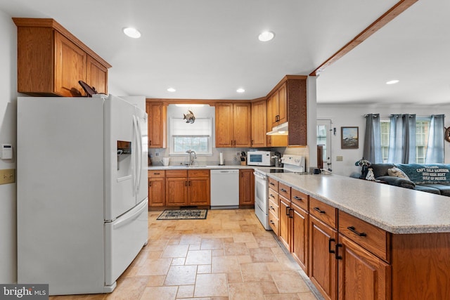 kitchen featuring under cabinet range hood, a peninsula, white appliances, open floor plan, and light countertops