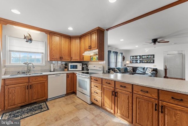 kitchen with white appliances, brown cabinets, open floor plan, under cabinet range hood, and a sink