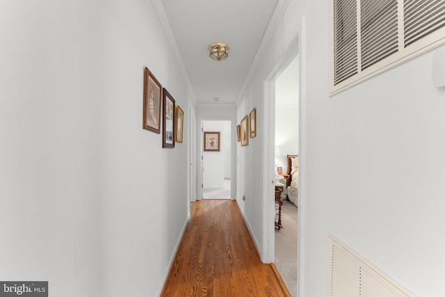 hallway featuring baseboards, wood finished floors, visible vents, and crown molding