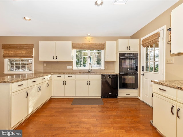 kitchen with sink, light hardwood / wood-style flooring, light stone counters, and black appliances