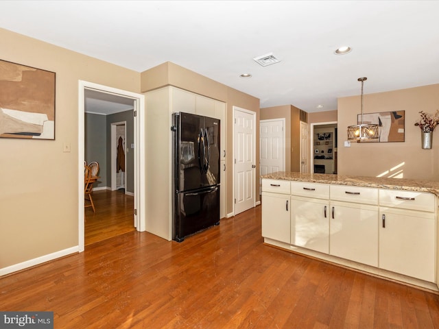 kitchen featuring pendant lighting, black refrigerator, light stone counters, and hardwood / wood-style floors