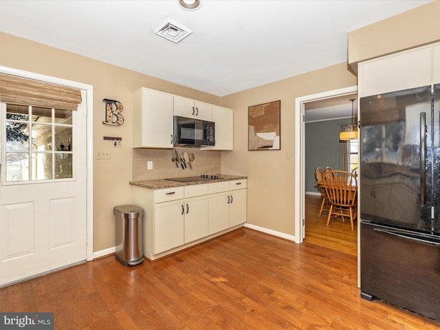 kitchen with tasteful backsplash, white cabinetry, light hardwood / wood-style flooring, and black appliances