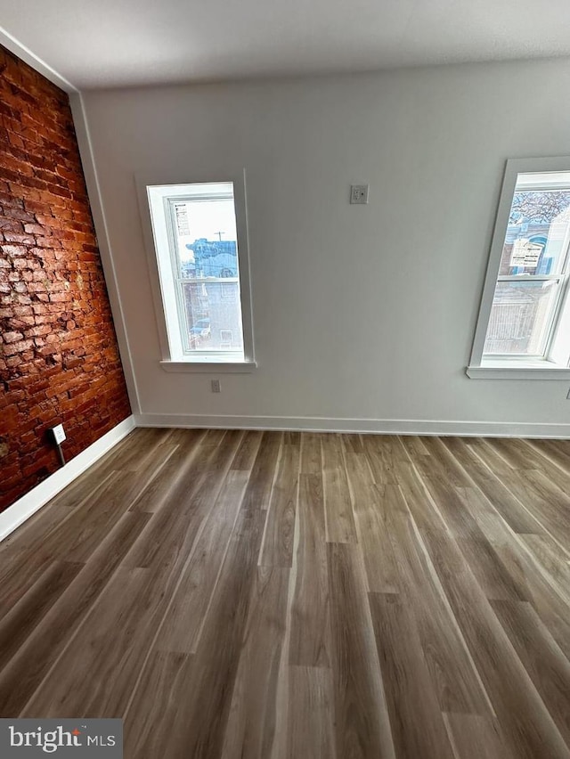 unfurnished room with dark hardwood / wood-style flooring, a healthy amount of sunlight, and brick wall