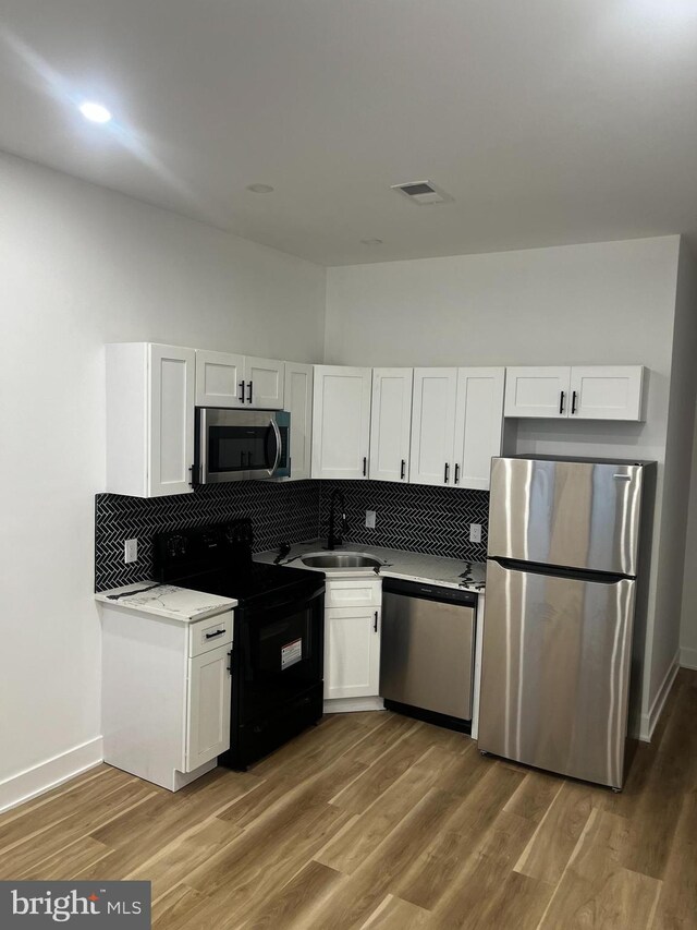 kitchen featuring backsplash, white cabinetry, hardwood / wood-style flooring, and appliances with stainless steel finishes