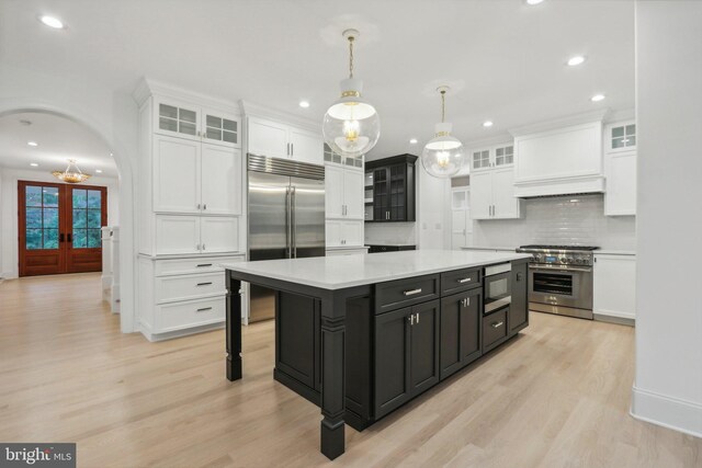 kitchen with backsplash, premium range hood, pendant lighting, built in appliances, and a kitchen island