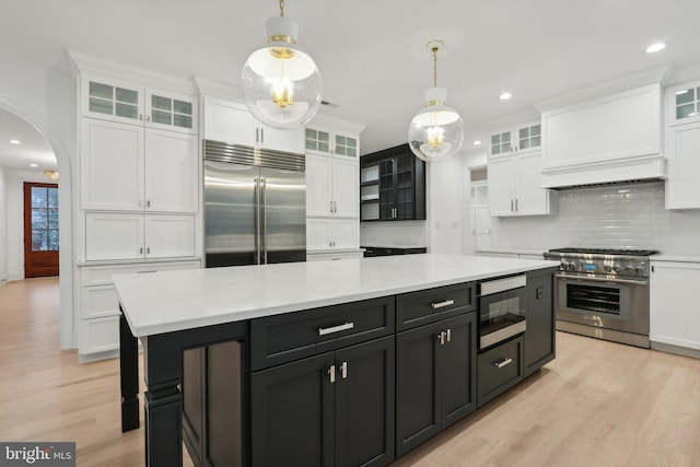 kitchen with decorative backsplash, a kitchen island, built in appliances, white cabinetry, and hanging light fixtures