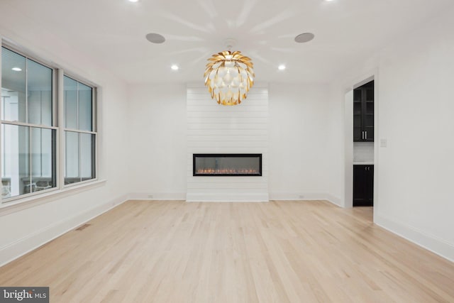 unfurnished living room with a fireplace, a chandelier, and light wood-type flooring