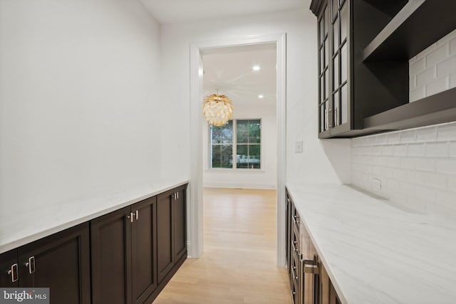 bar with a notable chandelier, dark brown cabinets, light stone countertops, and light hardwood / wood-style flooring