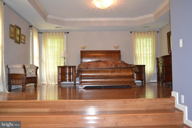 bedroom featuring a tray ceiling, wood finished floors, visible vents, and ornamental molding