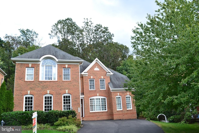 view of front of property with brick siding, driveway, and a shingled roof