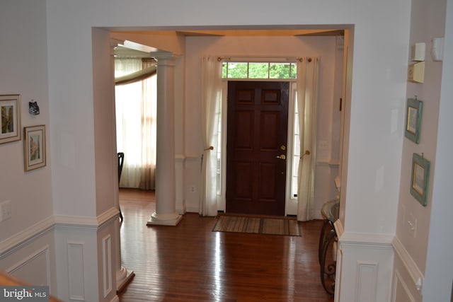 entryway with a wainscoted wall, a decorative wall, ornate columns, and wood finished floors