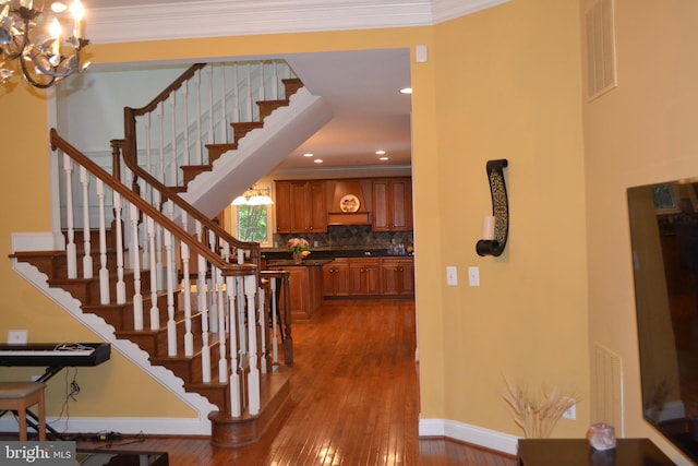 stairway featuring visible vents, ornamental molding, hardwood / wood-style flooring, baseboards, and a chandelier