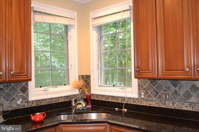 kitchen featuring backsplash, dark stone counters, brown cabinets, and a sink