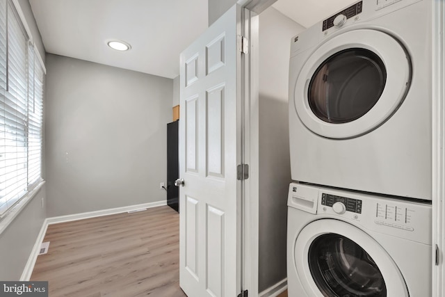 laundry area with light wood-type flooring and stacked washer / dryer