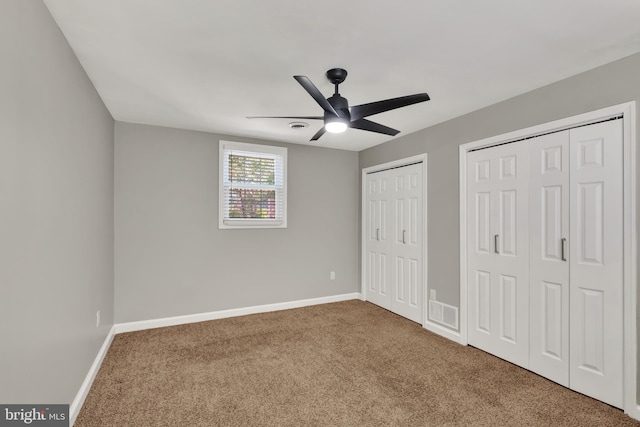 unfurnished bedroom with carpet flooring, multiple closets, and ceiling fan