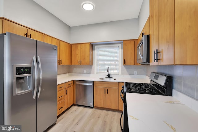 kitchen with backsplash, sink, stainless steel appliances, and light hardwood / wood-style flooring