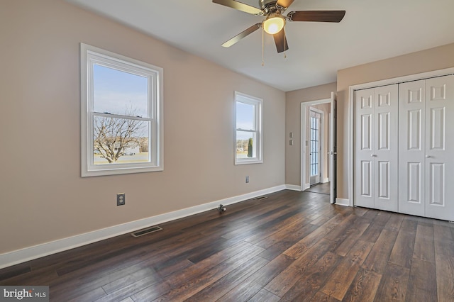 unfurnished bedroom featuring ceiling fan, dark hardwood / wood-style floors, a closet, and multiple windows