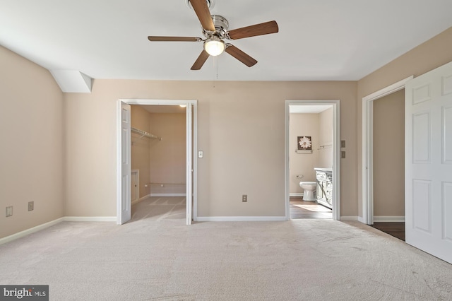 unfurnished bedroom featuring ceiling fan, a spacious closet, connected bathroom, light colored carpet, and a closet